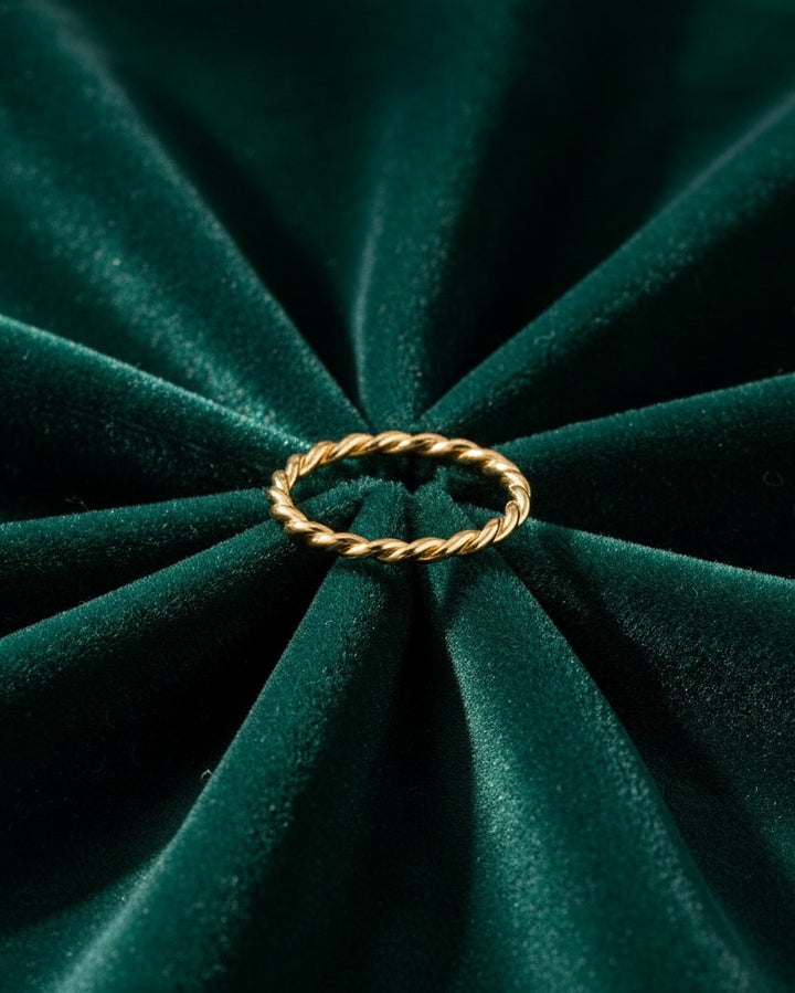 Elli Jewellery gold plated twisted rope band ring resting on a dark green velvet fabric background.