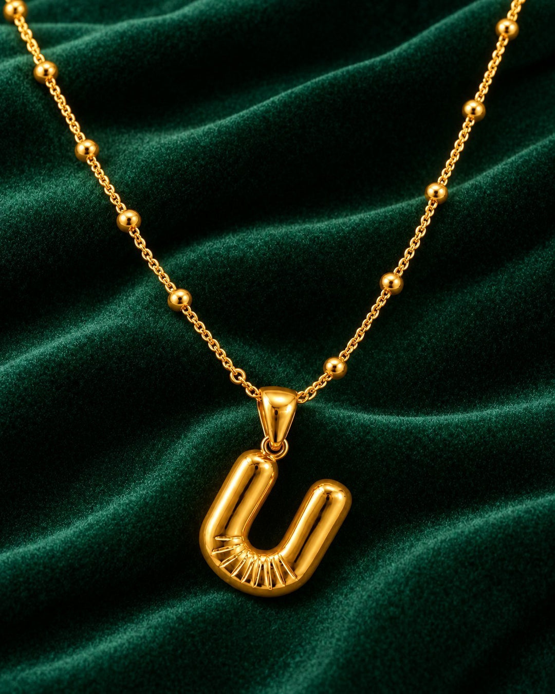 Elli Jewellery gold plated waterproof chunky chain necklace featuring a sculptural U initial pendant on green velvet.