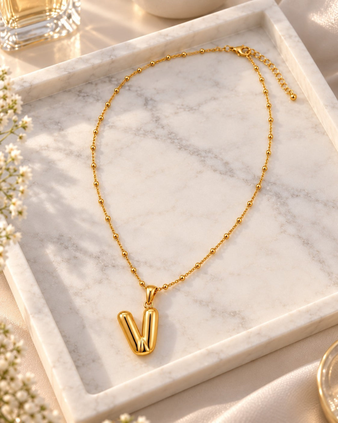 Elli Jewellery gold plated waterproof chunky V-shaped pendant necklace on a marble tray with soft sunlight.