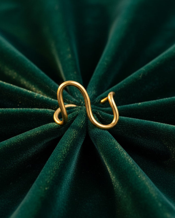 Elli Jewellery gold plated curved wave band ring on a dark green velvet background.
