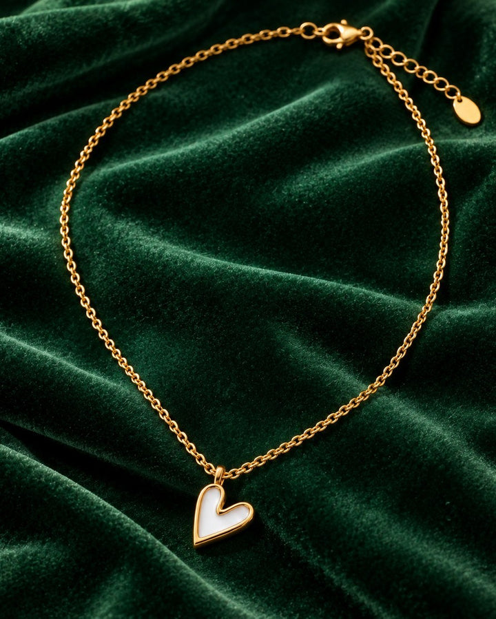 Elli Jewellery gold plated necklace featuring a white enamel heart pendant on a delicate chain against green velvet.