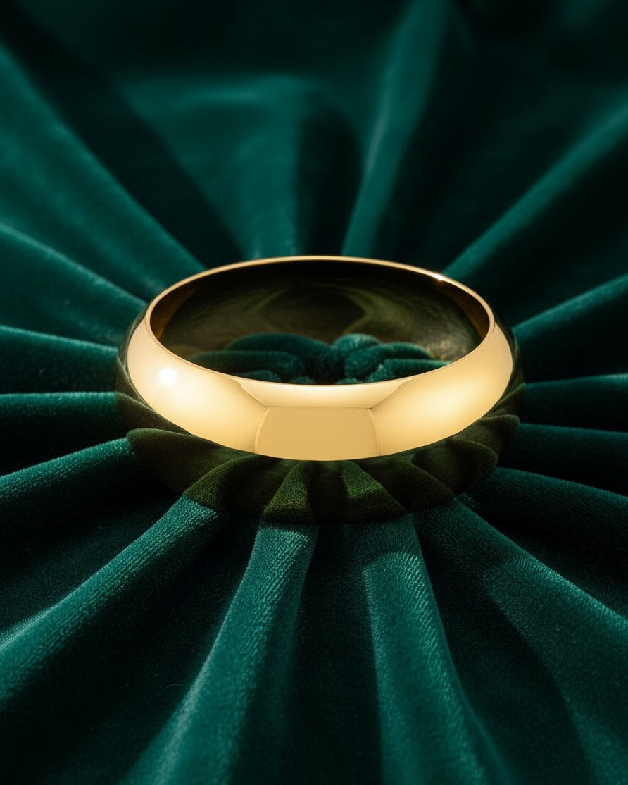 Elli Jewellery gold plated wide statement bangle with a smooth polished finish resting on dark green velvet fabric.