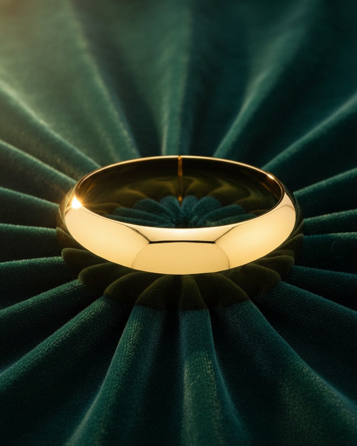 Elli Jewellery wide gold plated statement bangle bracelet with a polished finish resting on dark green velvet fabric.
