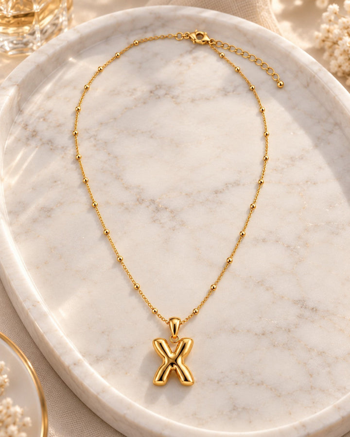 Elli Jewellery gold plated waterproof necklace featuring a chunky X-shaped pendant on a delicate beaded chain.