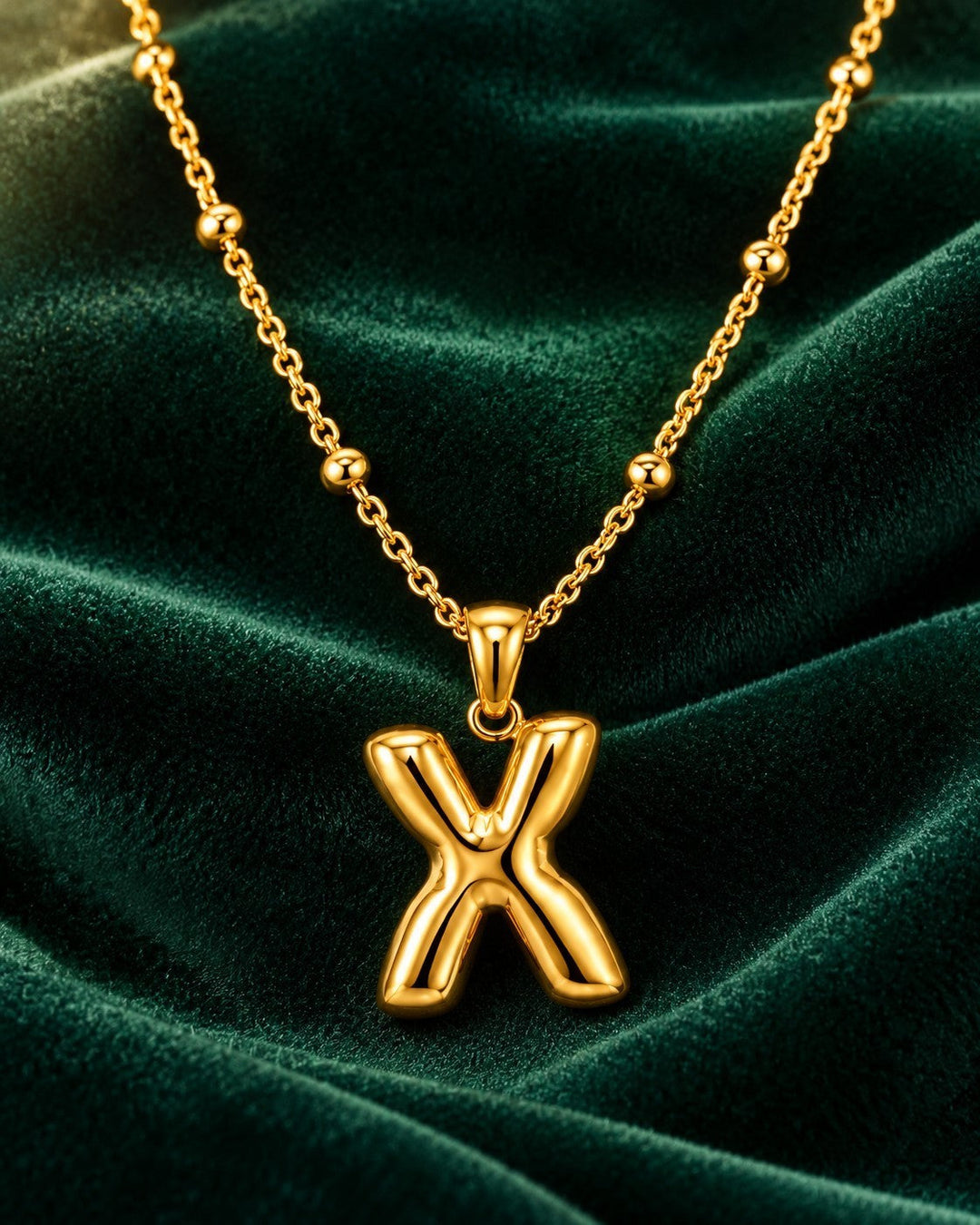 Elli Jewellery gold plated waterproof chunky X link pendant necklace on a dark green velvet background