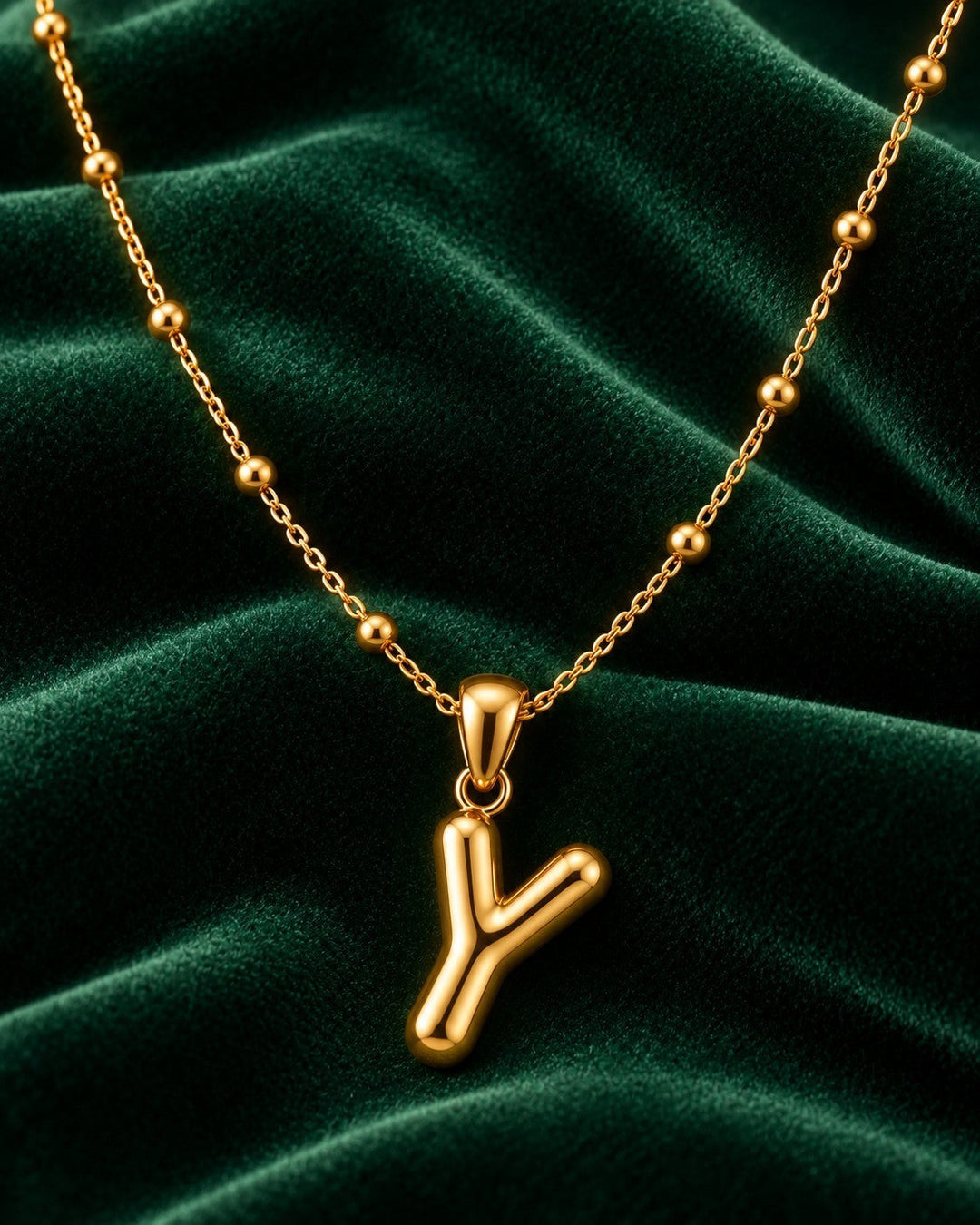 Elli Jewellery gold plated chunky Y-drop statement necklace with a beaded chain on a dark green velvet background