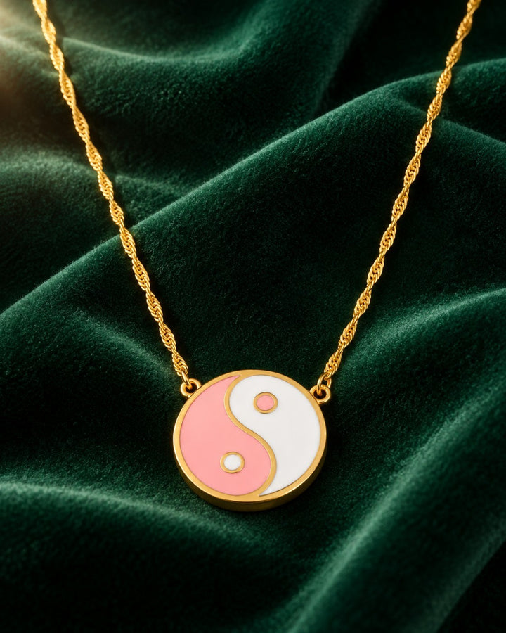 Elli Jewellery gold plated yin yang pendant necklace with pink and white enamel on a green velvet background