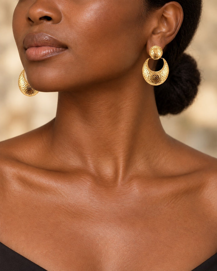 Model wearing Elli Jewellery hammered gold plated crescent drop earrings with a circular stud and textured finish.