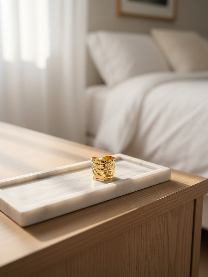 Elli Jewellery wide hammered gold plated adjustable ring resting on a white marble tray in a sunlit bedroom.