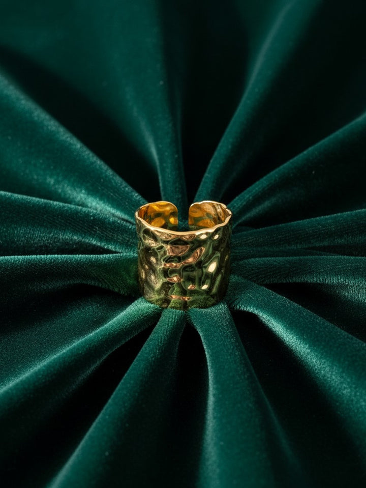 Elli Jewellery wide hammered gold plated adjustable ring resting on a dark green velvet background