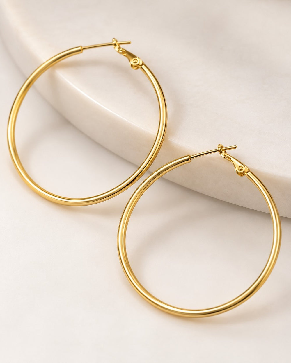Elli Jewellery large smooth 18ct gold plated hoop earrings resting on a white marble surface