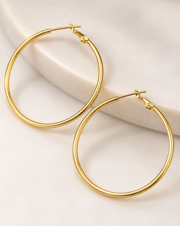 Elli Jewellery large smooth 18ct gold plated hoop earrings resting on a white marble surface