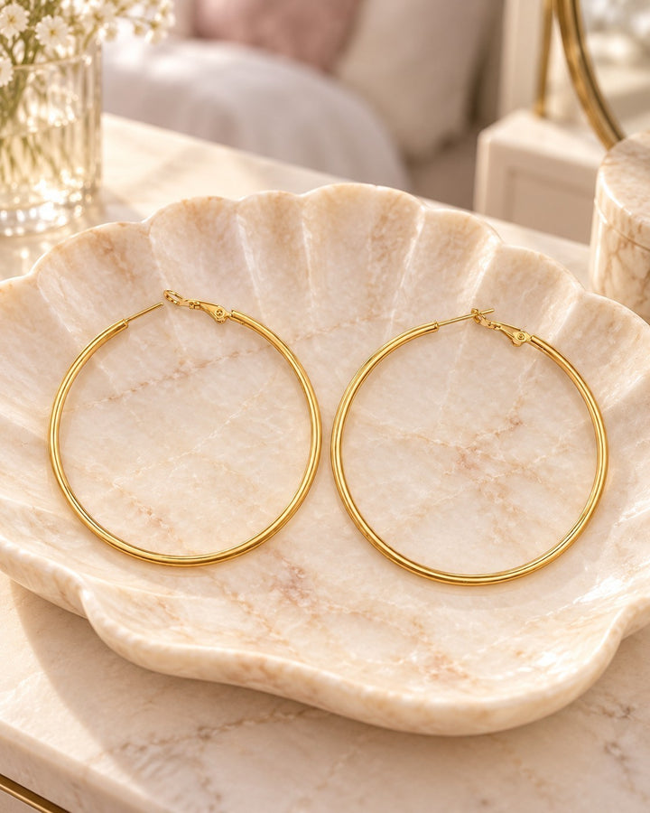 Elli Jewellery large smooth 18ct gold plated hoop earrings resting on a decorative marble shell dish.