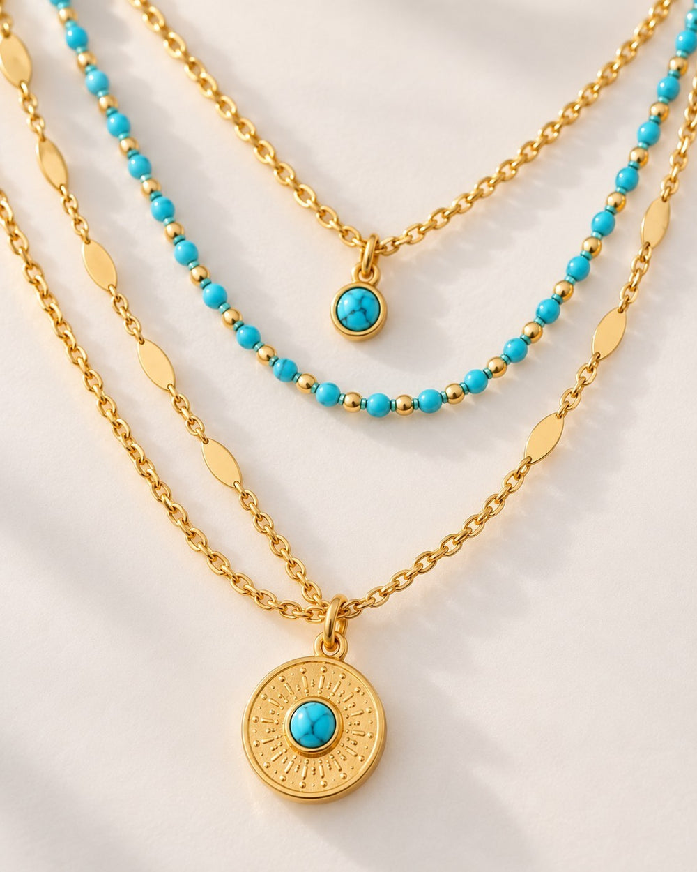 Elli Jewellery layered gold necklace with turquoise beads and a round sunburst pendant on a white background