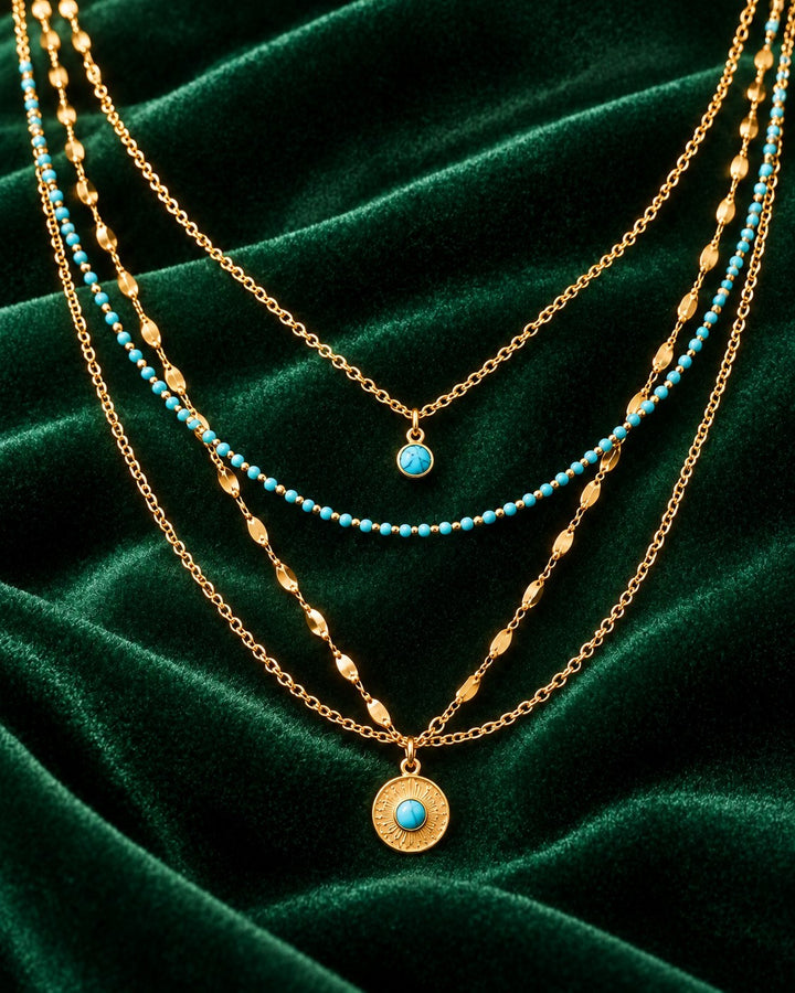 Elli Jewellery layered gold necklace featuring turquoise stone accents and sunburst pendant on green velvet