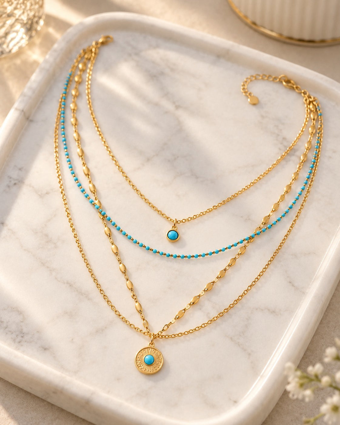 Elli Jewellery layered gold necklace featuring turquoise bead accents and a sunburst pendant on a marble tray