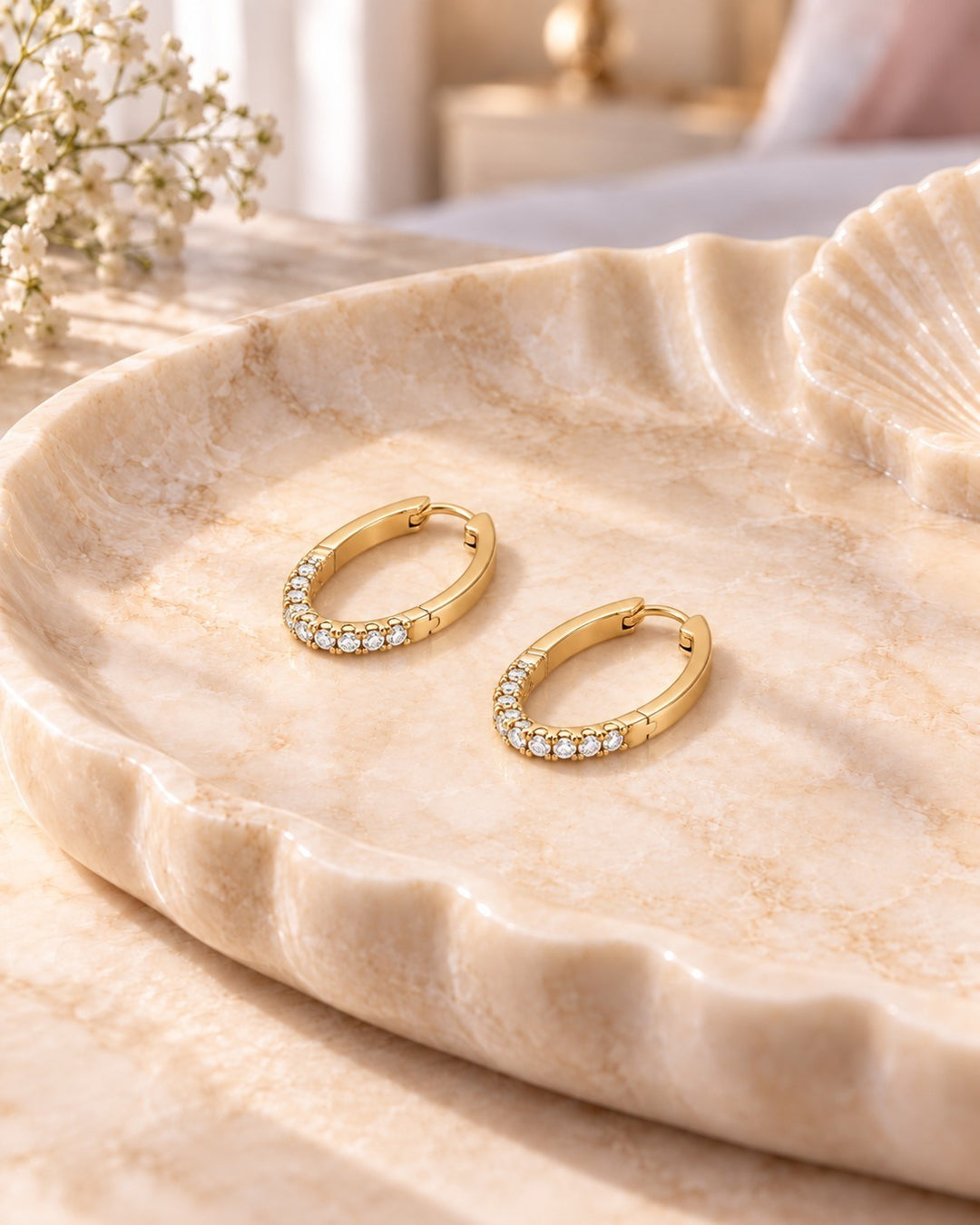 Elli Jewellery gold plated hoop earrings with pavé-set clear crystals resting on a decorative shell tray.