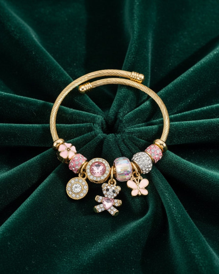 Elli Jewellery gold plated cuff bracelet featuring pink crystals, teddy bear, and flower charms on green velvet.