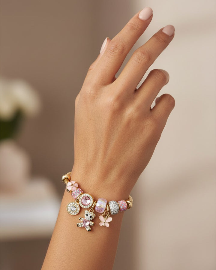 Elli Jewellery gold plated cuff bracelet with pink crystals, teddy bear, and butterfly charms on a woman's wrist.