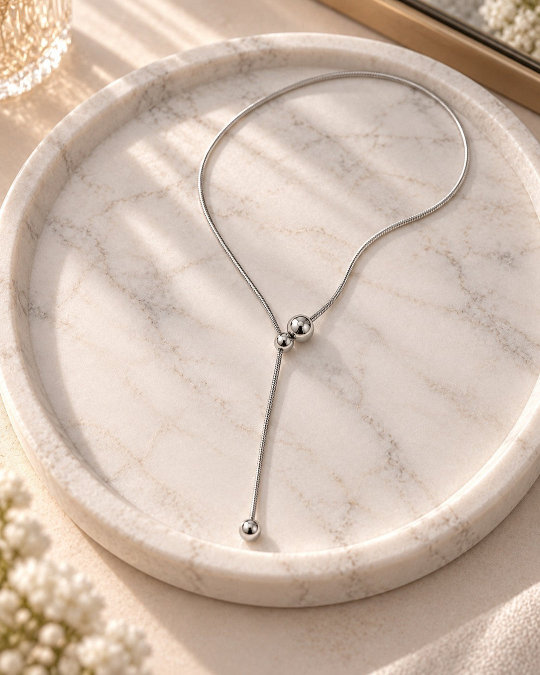 Elli Jewellery rhodium plated waterproof lariat ball chain necklace resting on a white marble tray in soft sunlight.