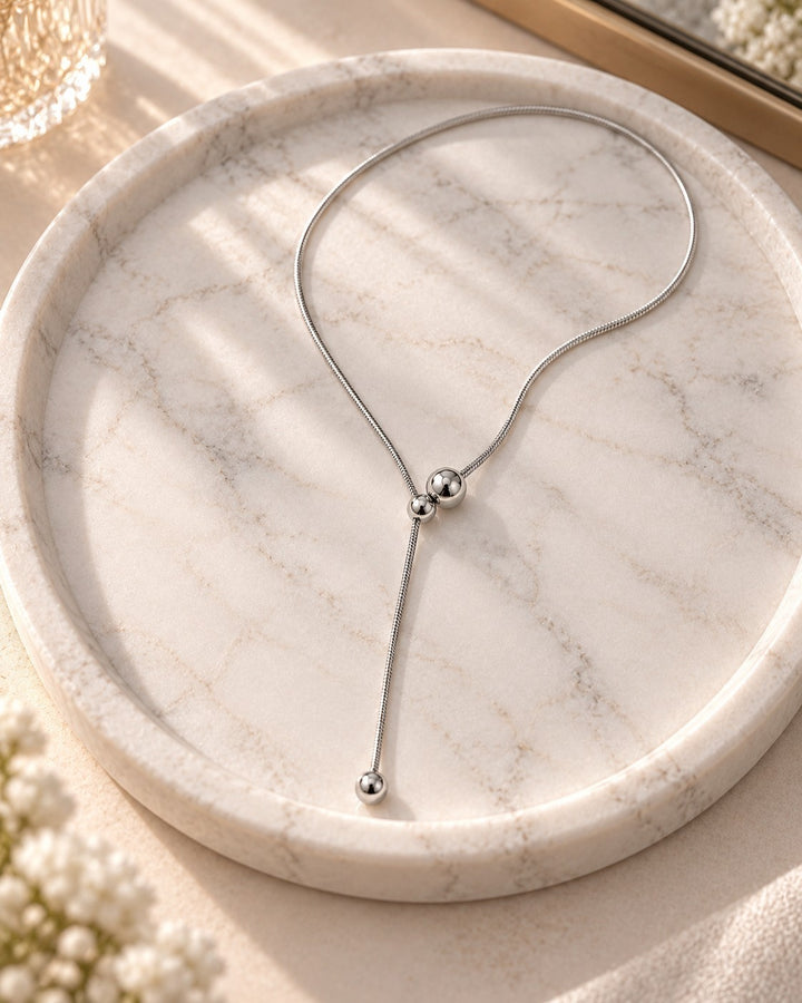 Elli Jewellery rhodium plated waterproof lariat ball chain necklace resting on a white marble tray in soft sunlight.