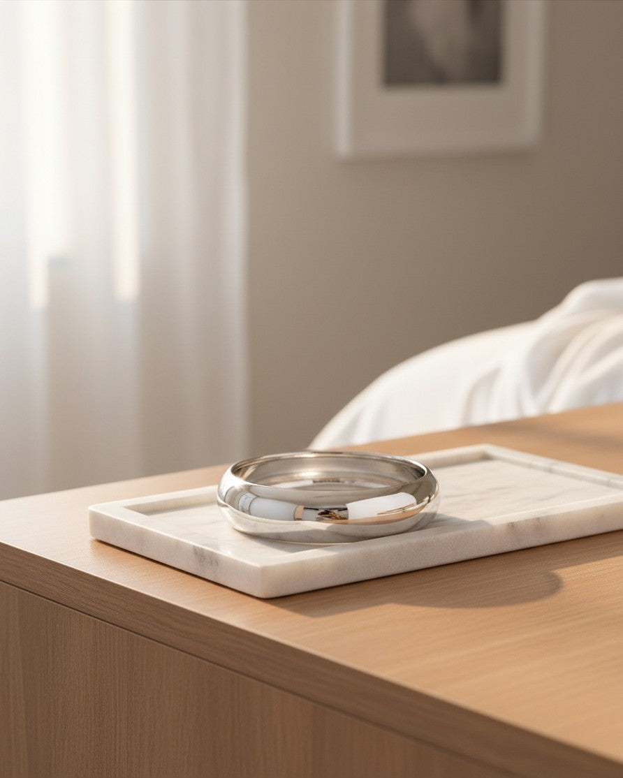 Elli Jewellery rhodium plated 2cm wide polished bangle bracelet resting on a white marble tray.