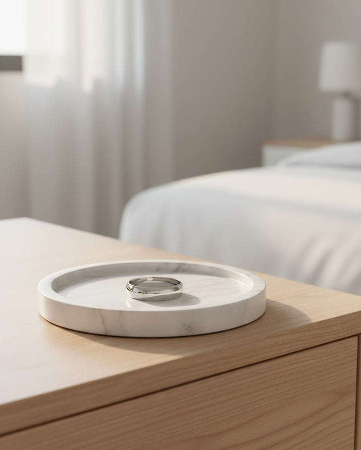 Elli Jewellery rhodium plated polished slim 1cm bangle bracelet resting on a white marble tray on a wooden table.