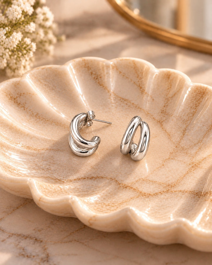 Elli Jewellery rhodium plated hollow C-shaped hoop earrings resting on a decorative shell-shaped dish.