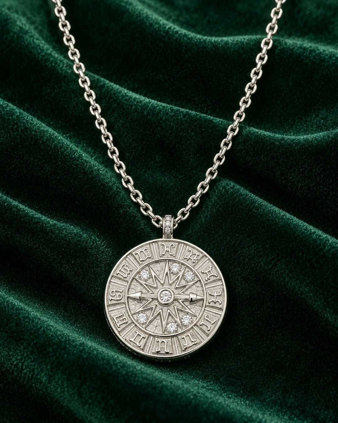 Elli Jewellery rhodium plated compass coin pendant necklace with crystal accents on a dark green velvet background