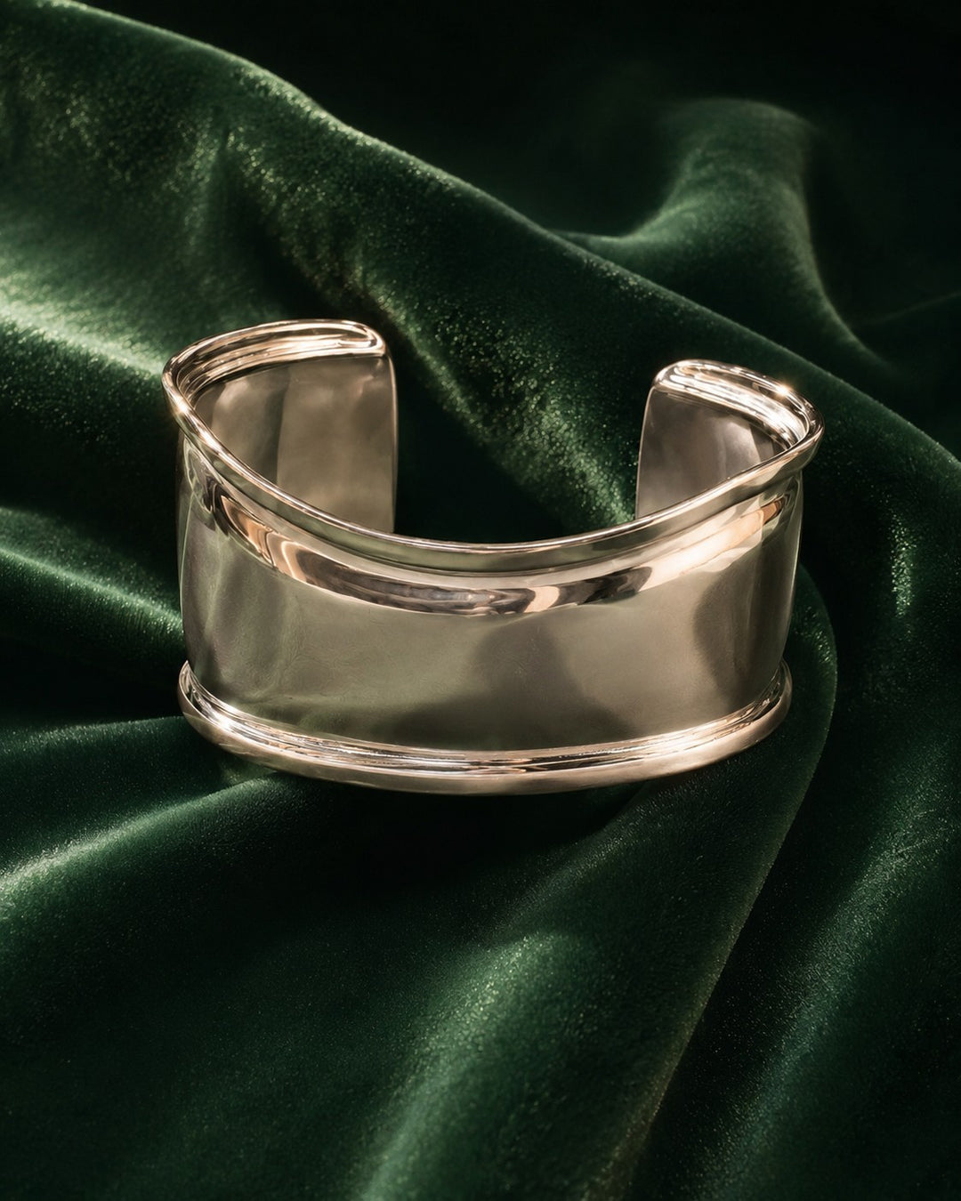 Elli Jewellery rhodium plated minimalist curved bangle bracelet resting on a luxurious dark green velvet fabric.