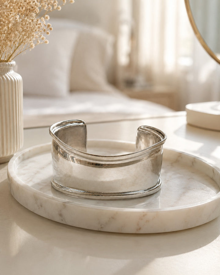 Elli Jewellery rhodium plated minimalist curved bangle bracelet on a marble tray in a bright, elegant bedroom setting.