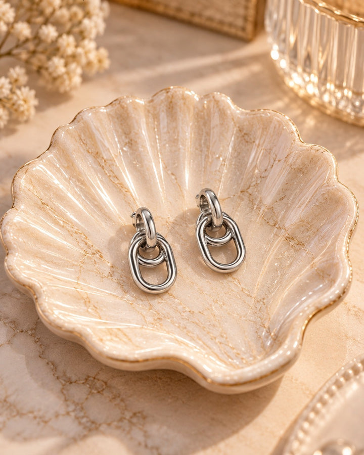 Elli Jewellery rhodium plated drop earrings with interlocking oval links resting in a decorative shell dish.