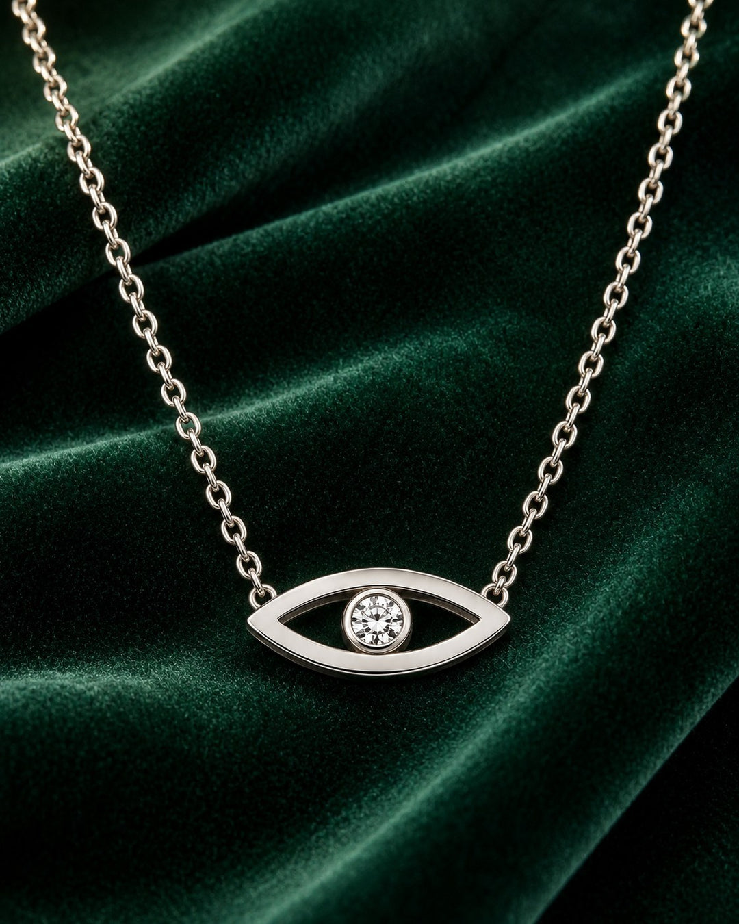 Elli Jewellery rhodium plated evil eye pendant necklace with a central cubic zirconia stone on a green velvet backdrop