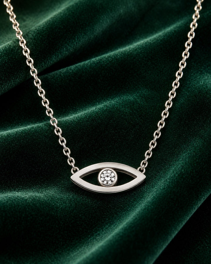 Elli Jewellery rhodium plated evil eye pendant necklace with a central cubic zirconia stone on a green velvet backdrop