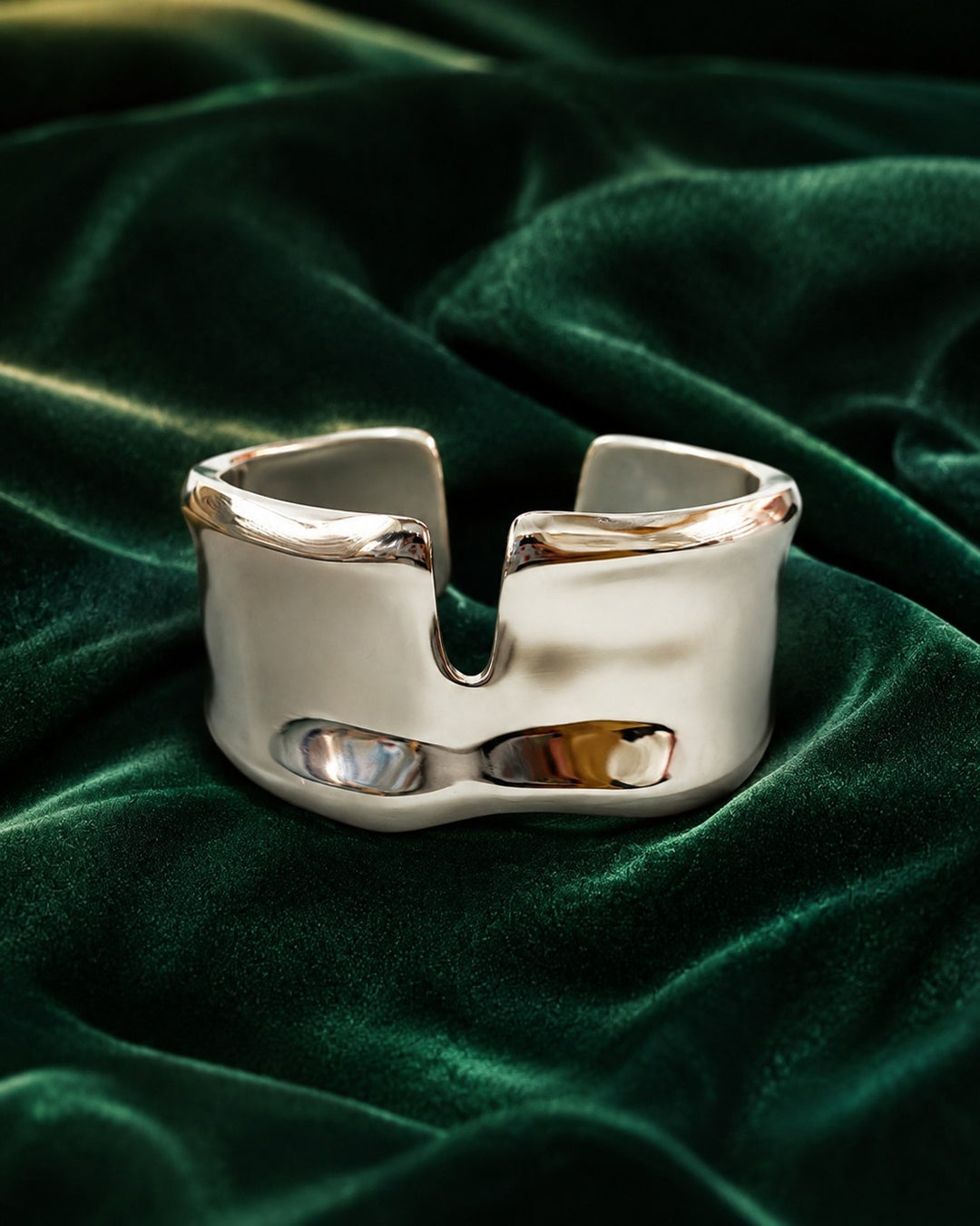 Elli Jewellery rhodium plated statement bangle with a hammered texture, displayed on a dark green velvet background.