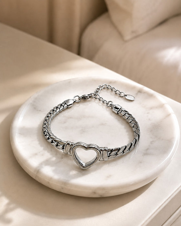 Elli Jewellery rhodium plated Cuban link bracelet featuring a central open heart charm on a marble display tray