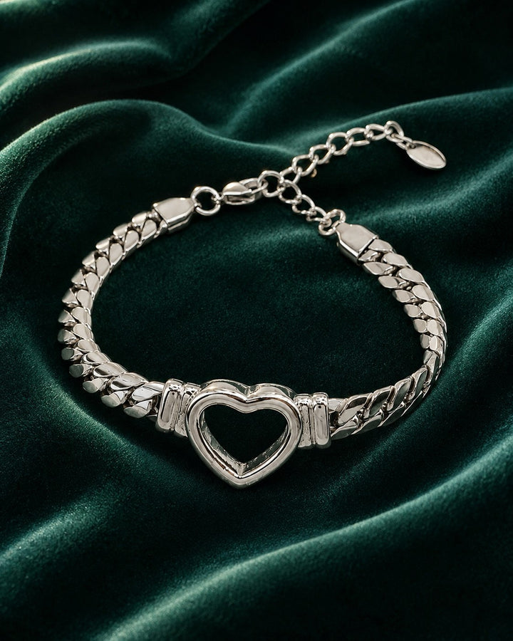 Elli Jewellery rhodium plated Cuban link bracelet featuring a central open heart charm on a dark green velvet background