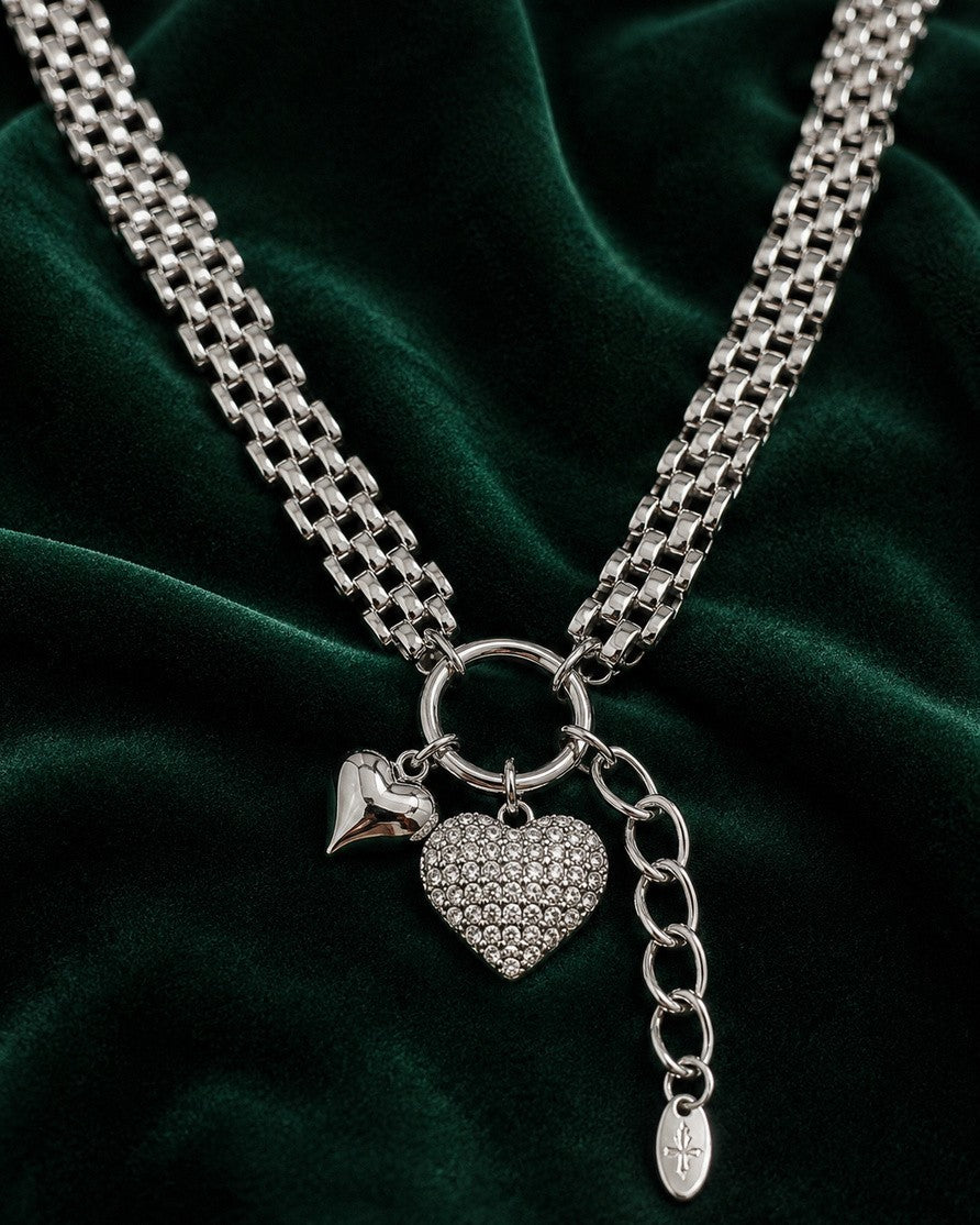 Elli Jewellery rhodium plated heart pendant necklace with a chunky chain on a dark green velvet background.
