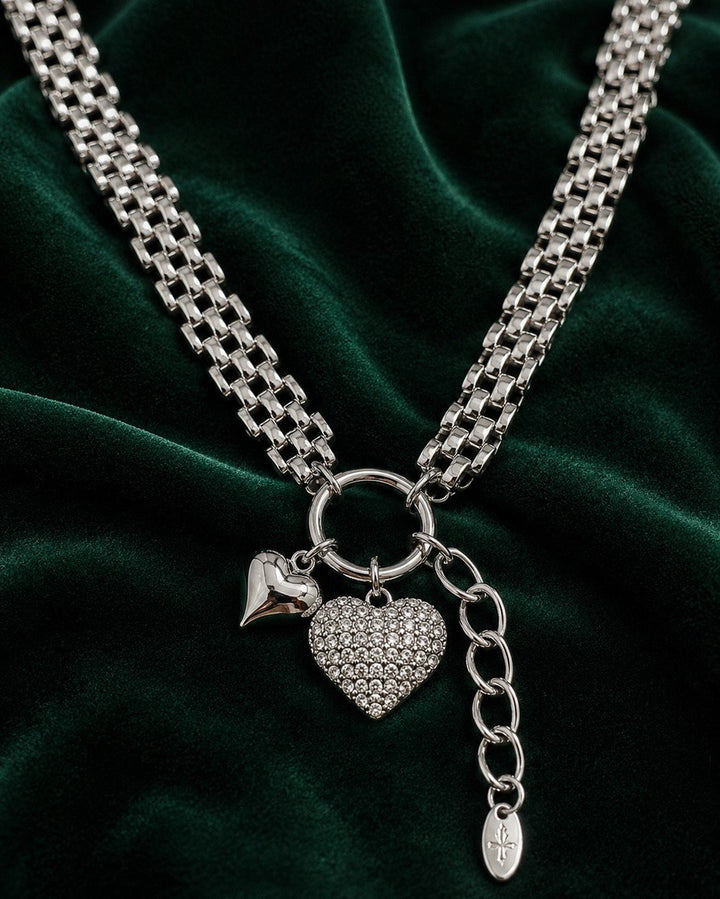 Elli Jewellery rhodium plated heart pendant necklace with a chunky chain on a dark green velvet background.