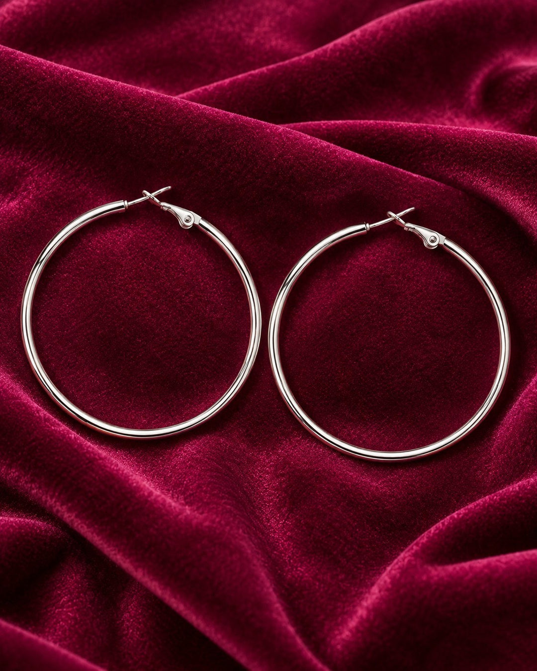 Elli Jewellery rhodium plated hoop earrings with a smooth polished finish resting on deep red velvet fabric
