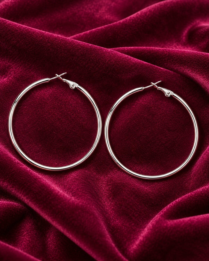 Elli Jewellery rhodium plated hoop earrings with a smooth polished finish resting on deep red velvet fabric