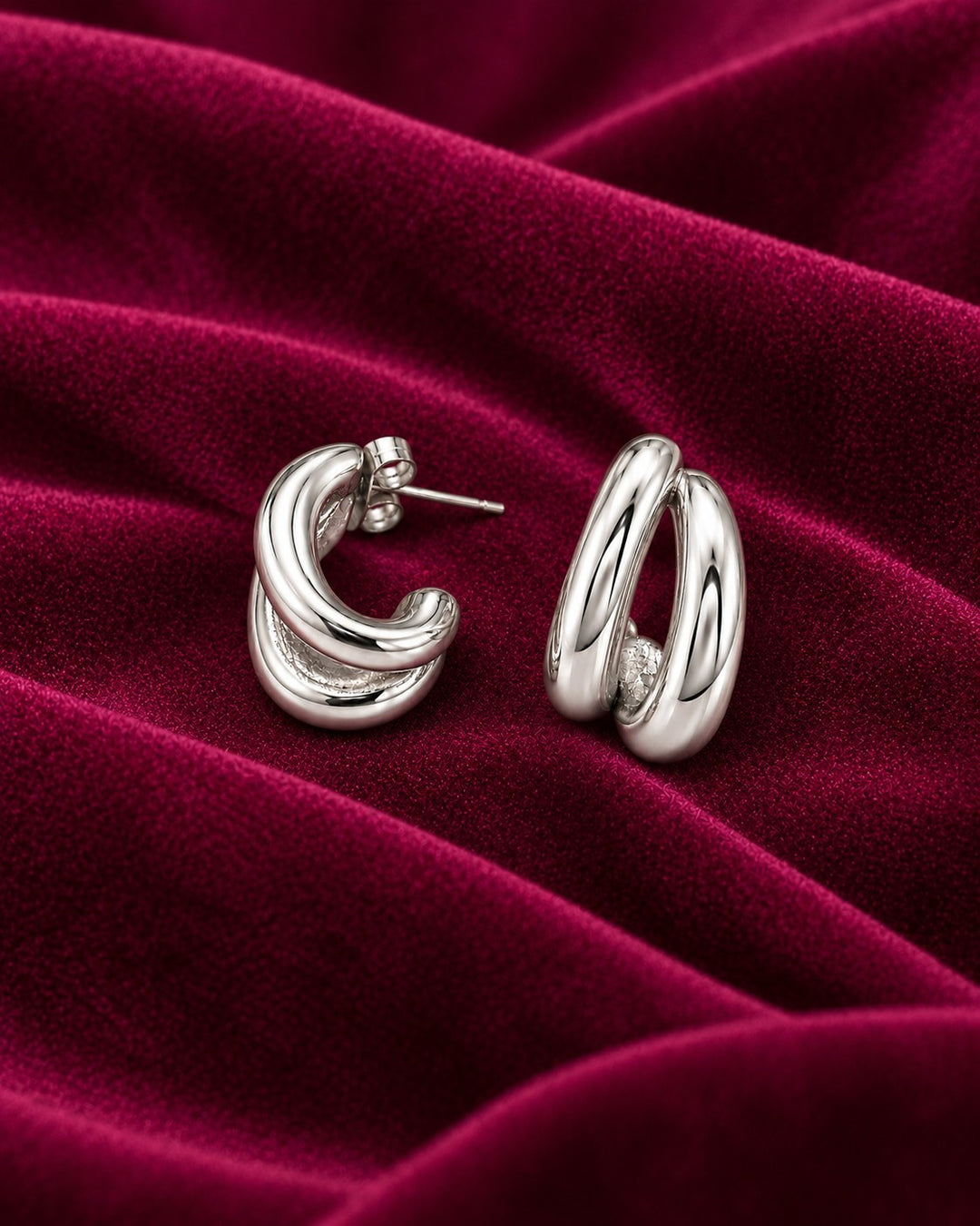 Elli Jewellery rhodium plated hollow C-shaped hoop earrings with a polished silver-tone finish on deep red velvet.