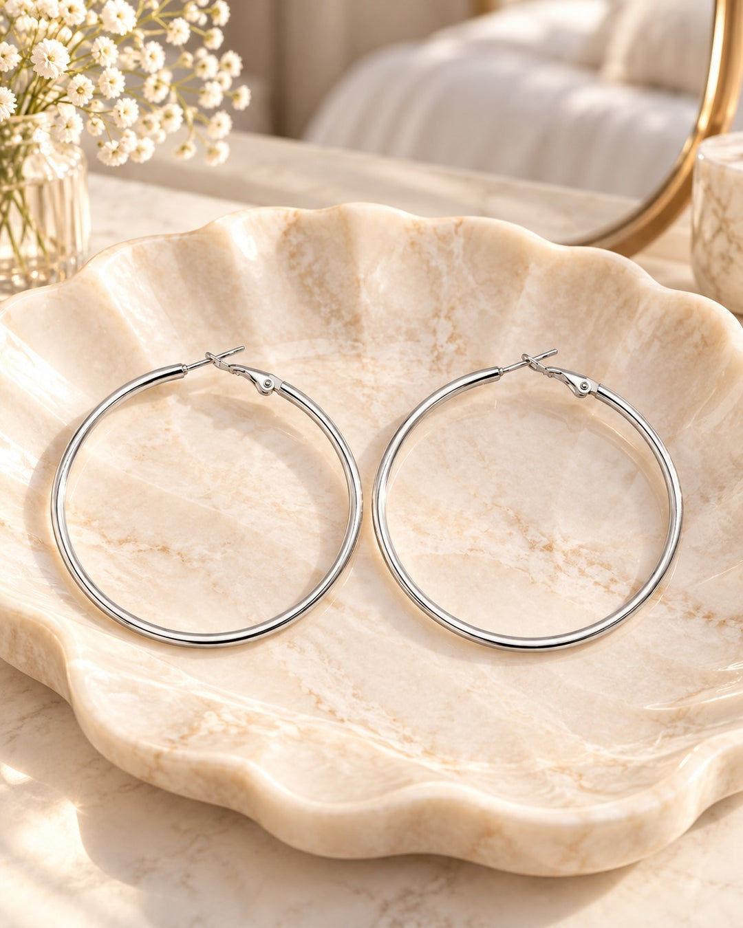 Elli Jewellery rhodium plated smooth hoop earrings resting on a decorative marble shell dish.