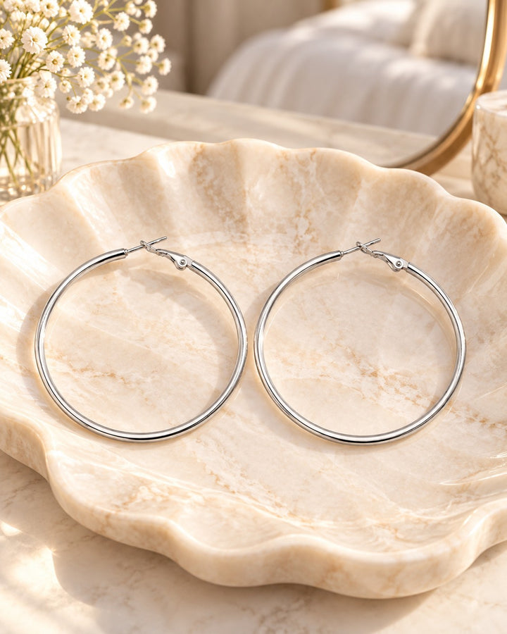 Elli Jewellery rhodium plated smooth hoop earrings resting on a decorative marble shell dish.