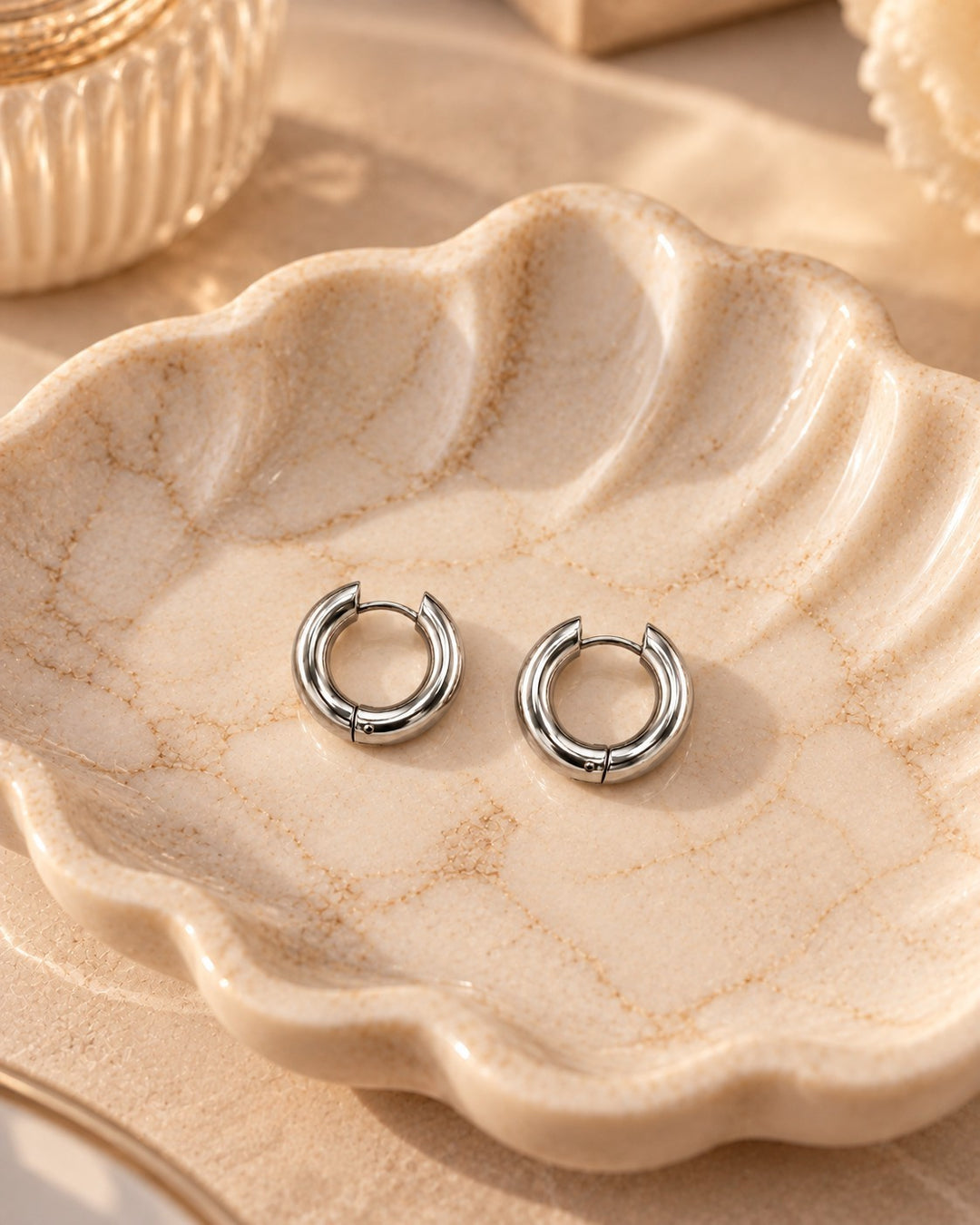 Elli Jewellery rhodium plated silver huggie hoop earrings resting on a decorative ceramic shell dish