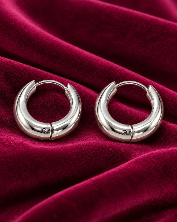 Elli Jewellery rhodium plated minimalist huggie hoop earrings on a luxurious deep red velvet background