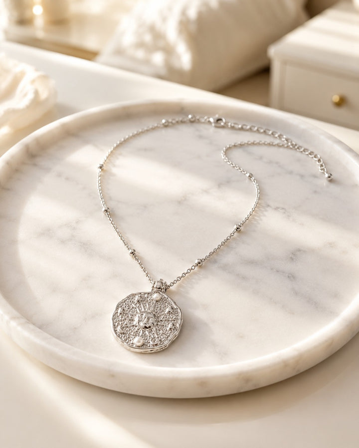 Elli Jewellery rhodium plated medallion necklace with sun motif and pearl accents on a marble tray
