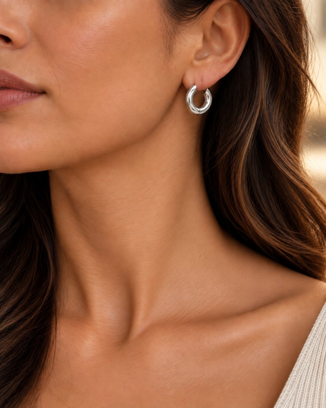 Model wearing Elli Jewellery rhodium plated waterproof mid huggie hoop earrings with a sleek silver finish
