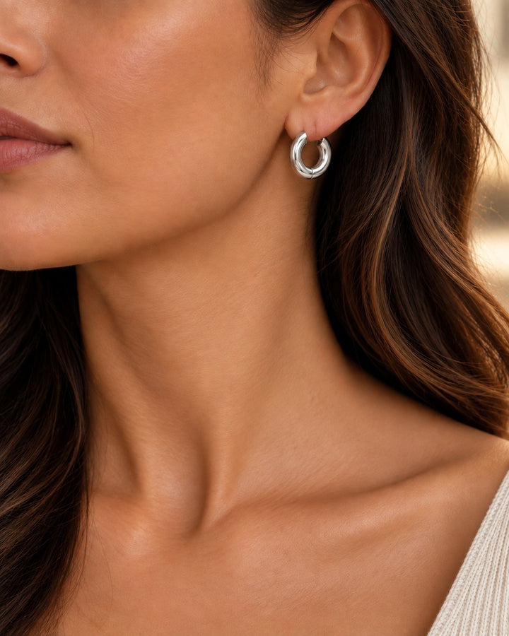 Model wearing Elli Jewellery rhodium plated waterproof mid huggie hoop earrings with a sleek silver finish