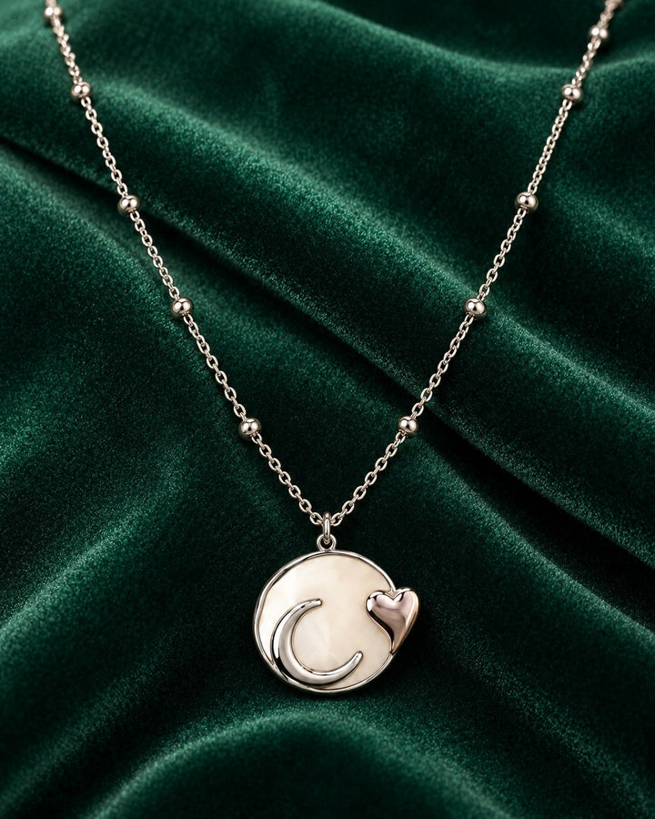 Elli Jewellery rhodium plated necklace featuring a moon and heart charm on a beaded chain against green velvet.